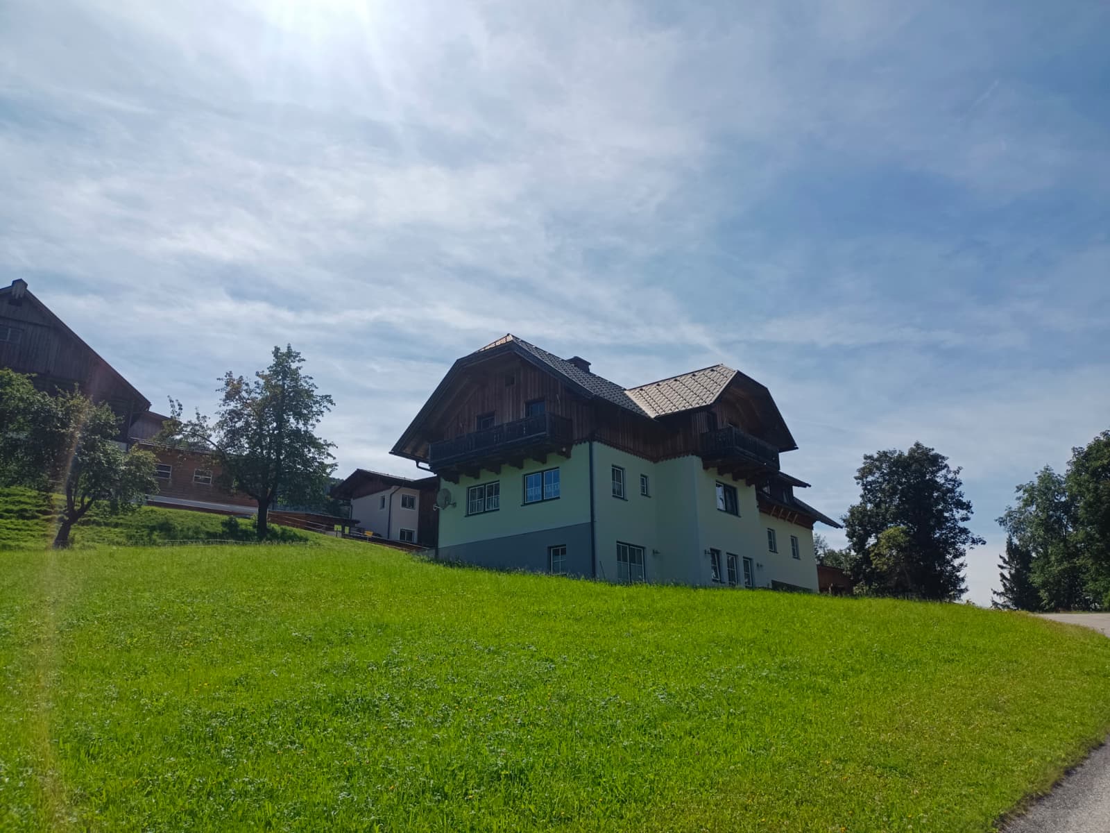 Ein Haus mit Schindeldach auf einem grünen Hügel unter blauem Himmel